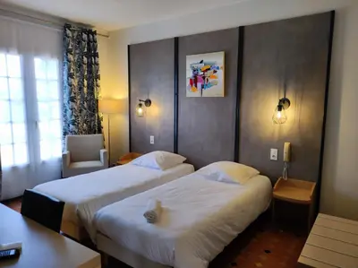 a hotel room with two beds and a chair at Hôtel et Appart'Hôtel Le Relais Du Val D'Orbieu in Ornaisons