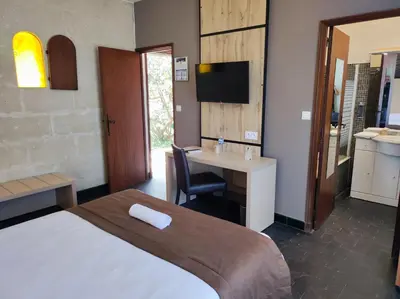 a bedroom with a bed and a desk and a television at Hôtel et Appart'Hôtel Le Relais Du Val D'Orbieu in Ornaisons