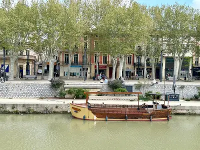 a boat sitting in the water next to a building at Le Victor Hugo de la Robine in Narbonne