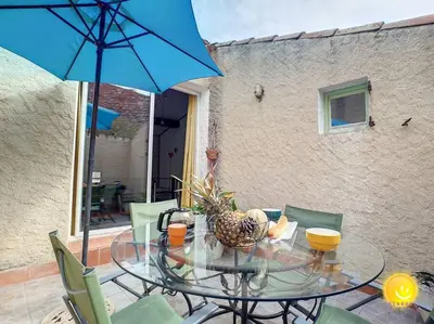 a glass table with chairs and a blue umbrella at Coeur de Fitou Maison de village atypique avec terrasse in Fitou