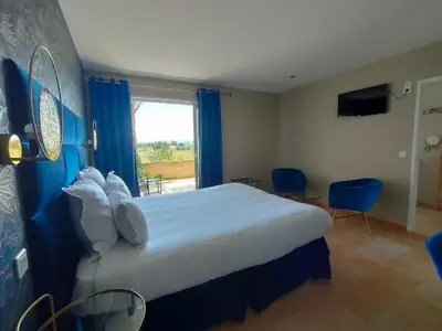 a bedroom with a large bed with blue curtains and a window at Hôtel Restaurant L'Art des Mets by Côté Jardin in Conilhac-Corbières