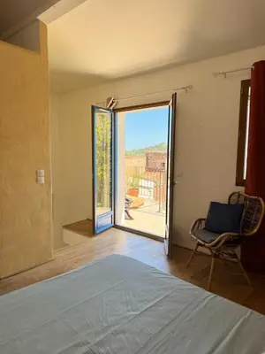 a bedroom with a bed and a chair and an open door at La vue de la calade in Peyriac-de-Mer
