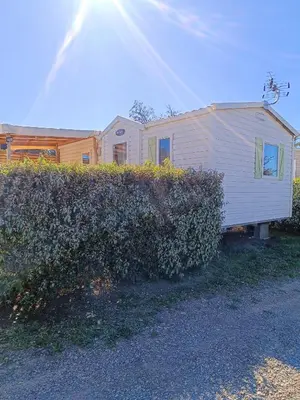 a white trailer is parked next to a hedge at MOBIL HOME LUCKY climatisé camping PORT LA NOUVELLE in Port-la-Nouvelle