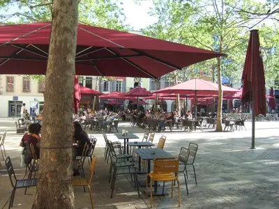a group of tables and chairs under a red umbrella at Appartement CarcaLuxe in Carcassonne