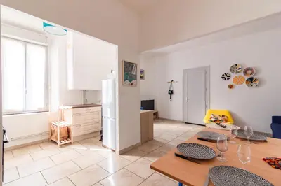 a living room with a table and a kitchen at Le Cerisier des 4 Chemins - Appt 75m² pour 6 in Carcassonne