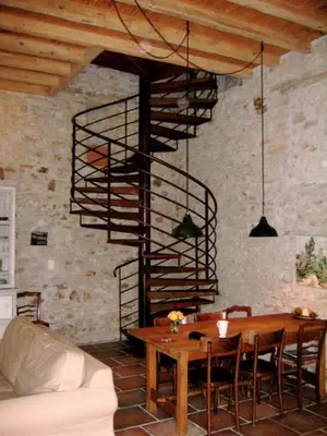 a living room with a wooden table and a spiral staircase at Le Clos Sainte Marie - Caune in Cenne-Monestiès
