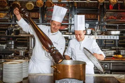 two chefs in a kitchen preparing food in a pot at Le Bambou Wifi Proche des pontons et du Doul in Peyriac-de-Mer