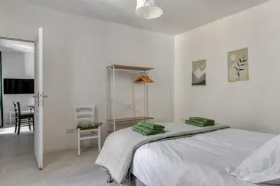 a white bedroom with a bed and a chair at Le Cyperus Appartement avec Terrasse et Wifi in Peyriac-de-Mer
