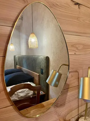 a mirror on a wooden wall with a bed and a chair at Parenthèse en Forêt - Gîte Hautbois, Sidobre in Le Bez