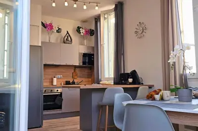 a kitchen with white cabinets and a table with chairs at L'Orchidée, proche de la gare avec clim et terrasse in Narbonne