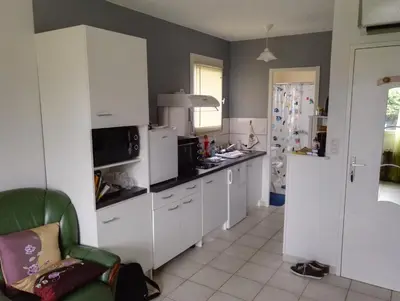 a kitchen with white cabinets and a green chair at Studio Tranquille in Castres