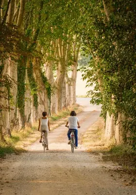 two people riding bikes down a dirt road with trees at Le Domaine de Camboyer, The Originals Collection in Montferrand