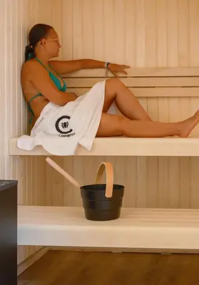 a woman sitting in a sauna with a bucket at Le Domaine de Camboyer, The Originals Collection in Montferrand