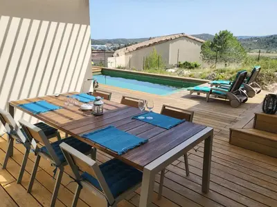 a wooden table and chairs on a deck with a pool at Villa contemporaine avec piscine in Montredon