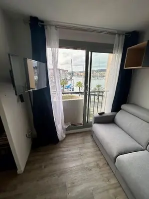 a living room with a couch and a large window at Superbe Studio avec vue sur le port de Gruissan, piscine, parking in Gruissan