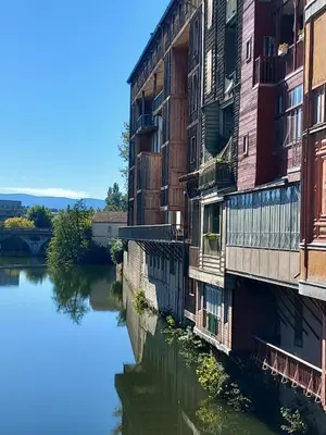 a building next to a river with reflections in the water at Chambre d'hote la passerelle in Mazamet
