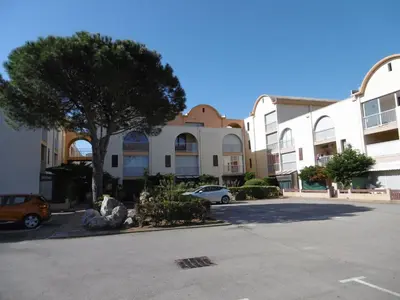 a car parked in a parking lot next to a building at **Gruissan : T2 cosy avec piscine, parking privé, proche plage et commerces** - FR-1-796-8 in Gruissan