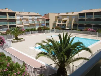 a resort swimming pool with a palm tree and buildings at T2 RDC avec Terrasse, Piscine & Parking - Proche Vieux Village de Gruissan - FR-1-796-20 in Gruissan