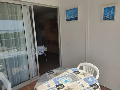 a table and chairs in a room with a balcony at Gruissan - Appartement climatisé - 6 pers - Parking - Plage à 50m - FR-1-796-51 in Gruissan