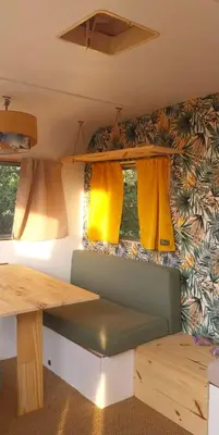 a table and a bench in a trailer with windows at La Caravane d'Alon in Magrie