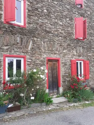 a stone building with red windows and a door at Au Grand Mûrier in Roquefère