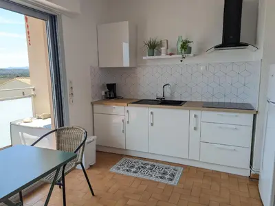 a kitchen with white cabinets and a table and a table and chair at Bel appartement T2 climatisé avec piscine et parking à 250m de la plage - FR-1-797-9 in Port-la-Nouvelle