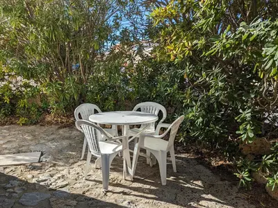 a white table and chairs sitting next to a bush at Agréable T2, 4 pers, plain-pied ouvert sur terrasse, jardin clos, parking privé, proche plage et commerces - FR-1-797-24 in Port-la-Nouvelle