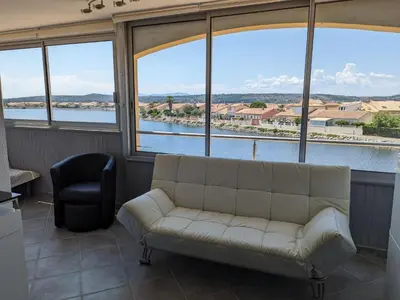 a living room with a couch and large windows at Grand T2 Climatisé 36m² avec Parking à 450m de la Plage - 4 Pers - FR-1-797-34 in Port-la-Nouvelle