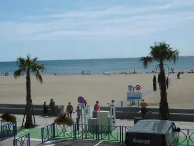 a beach with palm trees and people standing on the beach at Appartement T2 Front de Mer avec Balcon et Parking – Confort et Activités à Proximité - FR-1-797-37 in Port-la-Nouvelle