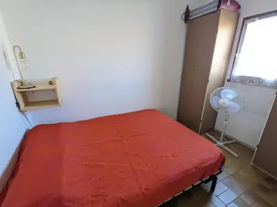 a bedroom with a red bed and a window and a fan at Villa T3 Mezzanine Climatisée, Proche Plage, Parking et Terrasse - 6 Pers - FR-1-797-56 in Port-la-Nouvelle