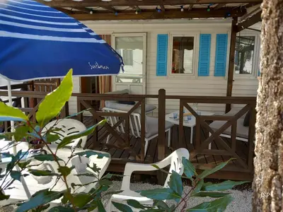 a porch with chairs and an umbrella in front of a house at Mobilhome Les volets bleus in Vaudreuille