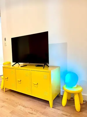 a yellow entertainment center with a television and a blue chair at Evasion dépaysante Canal du Midi La vie en couleur in Castelnaudary