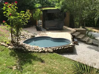 a swimming pool with rocks around it in a yard at Bus atypique au bord du canal du midi et au cœur d'une forêt 2 chambres in Villepinte