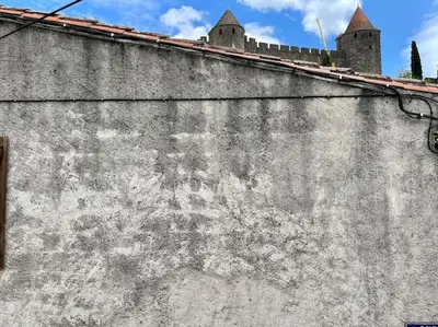 an old concrete wall with a castle in the background at La Tour de Guet in Carcassonne
