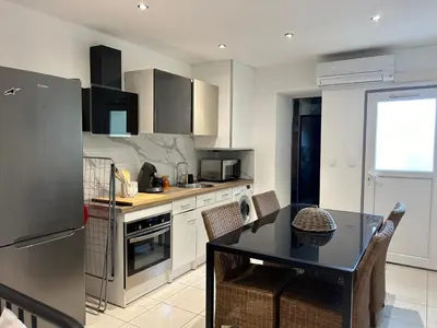 a kitchen with white cabinets and a table with chairs at Grand T2 climatisé avec jardin et spa in Narbonne
