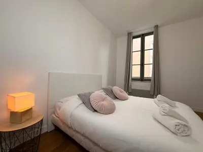 a white bedroom with a bed with pillows and a window at Le Moderniste Proche des Halles et Cathédrale in Narbonne