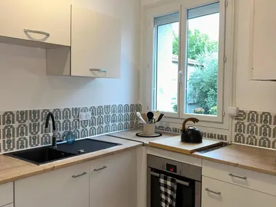 a kitchen with white cabinets and a sink and a window at Spacieux T2 climatisé Narbonne - Près du centre ville in Narbonne