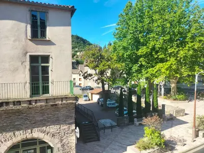 a building with a balcony next to a tree at Appartement le petit bonheur in Saint-Pons-de-Thomières