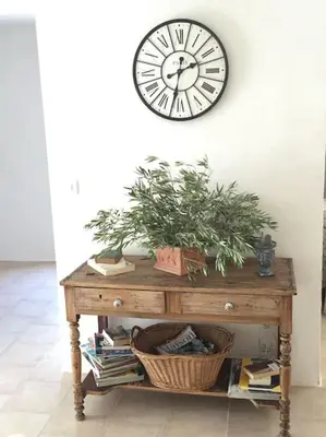 a clock on a wall above a table with a plant at Superbe maison de village et sa terrasse panoramique in Oupia