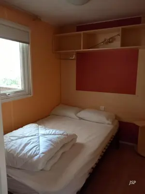 a bedroom with a bed with white sheets and a window at Mobil-home Riviera in Vaudreuille