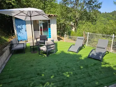 a group of chairs and an umbrella on a lawn at Gîte rural 8 à 10 personnes au coeur du Parc National du Haut Languedoc in Saint-Pons-de-Thomières