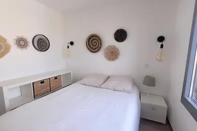 a white bedroom with a bed and some hats on the wall at La Gruissanaise in Gruissan