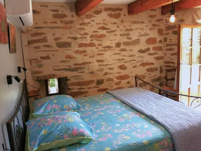 a bedroom with a bed and a stone wall at Gîte des Orangers in Roquebrun