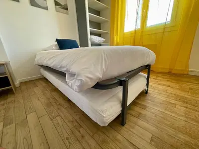 a bed in a room with white sheets and a wooden floor at Maison Les Bruyères - 3 chambres - jardin et parking à Carcassonne in Carcassonne