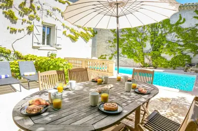 a wooden table with food and an umbrella on a patio at Villa La Fontaine by Villa Plus in Capestang