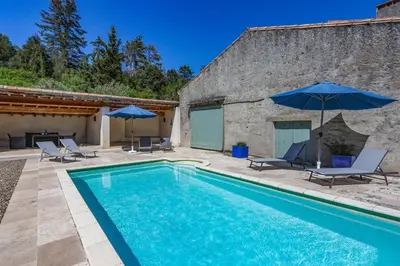 a swimming pool with chairs and umbrellas next to a building at Villa Domaine Saint Roch by Villa Plus in Gaja-et-Villedieu