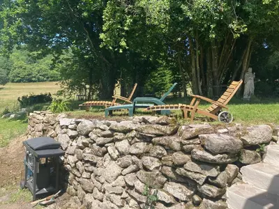 a stone wall with three wooden chairs and a fence at Maison NATURALY in Laprade