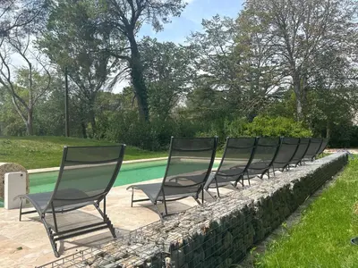 a row of chairs sitting on a stone wall next to a pool at Gîte les Mercieres la Villa Maison campagne grands espaces oasis de nature, convivialité, détente 5 Chambres piscine chauffée Wifi piano billard in Pexiora