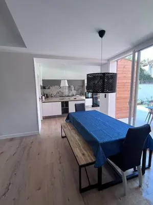 a living room with a blue table and a kitchen at Maison climatisée, piscine, à 5 minutes des Grands Buffets in Narbonne