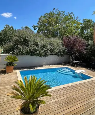a swimming pool in a yard with a wooden deck at La Tuilerie du Bazalac in Trèbes